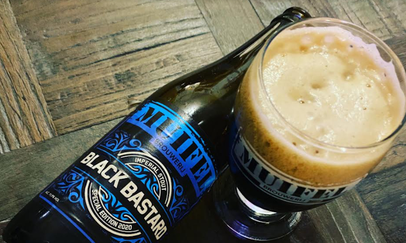 Black Bastard 2020 van Muifelbrouwerij flesje op tafel liggend naast een glas met het bier